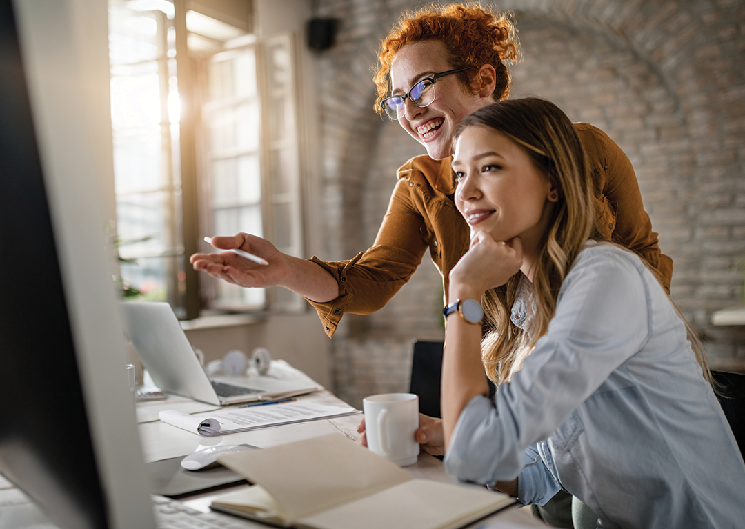 happy-female-entrepreneurs-reading-email-computer-while-working-together-office-focus-is-redhead-woman